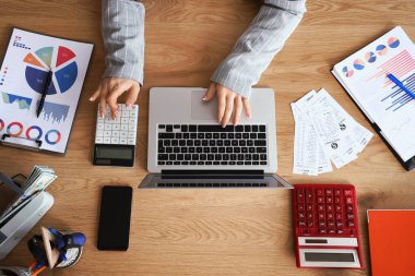 Dizüstü bilgisayar ve hesap makinesiyle çalışan kadın muhasebecinin elleri.