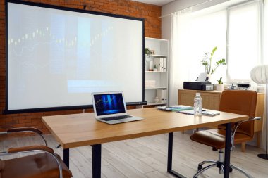 Ofisteki projektör ekranında ve tablo üzerinde döviz kurlarının diyagramları olan dizüstü bilgisayar