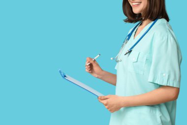 Mavi arka planda steteskobu ve panosu olan mutlu bir kadın kardiyolog.