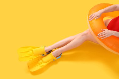 Sarı arka planda yüzme yüzüğü olan yüzgeçli kadın turist.