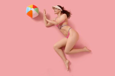 Pembe arka planda plaj topuyla mayo giymiş kadın turist.