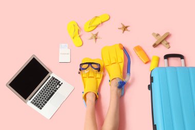 Plaj aksesuarları ve pembe arka planda boş dizüstü bilgisayarı olan kadın bacakları.