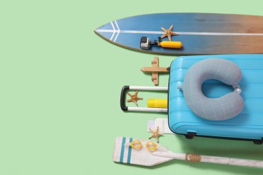 Yeşil arka planda seyahat aksesuarları ve sörf tahtaları olan bavul