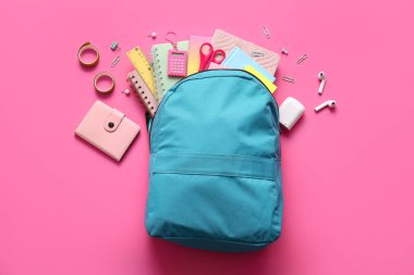 Mavi okul çantası, farklı kırtasiye malzemeleri ve pembe arka planda modern kulaklıklar.