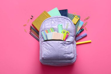 Pembe arka planda farklı kırtasiye malzemeleriyle leylak rengi okul çantası.