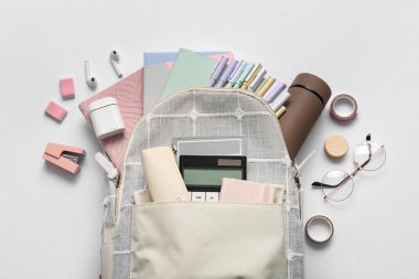 Farklı kırtasiye malzemeleri ve gri arka planda modern kulaklıklar olan şık bir okul çantası.