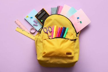 Sarı okul çantasının üzerinde farklı kırtasiye malzemeleri var.