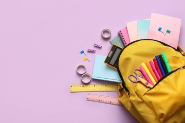 Sarı okul çantasının üzerinde farklı kırtasiye malzemeleri var.