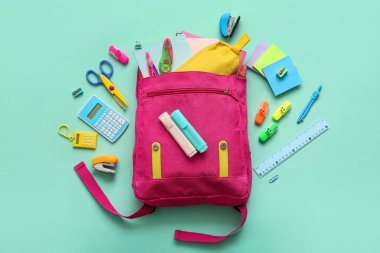 Pembe okul çantası ve turkuaz arka planda farklı kırtasiye malzemeleri.