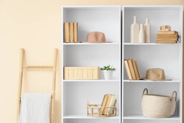 Bej duvarın yanında dekor ve merdiven olan kitaplık.