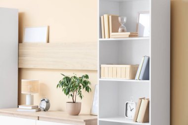 Odada bej duvarın yanında kum saati ve saatli kitaplık.