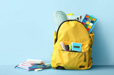 Mavi arka planda farklı kırtasiye malzemesi olan okul çantası