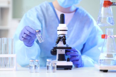 Ampule ve mikroskobu olan kadın bilim adamı laboratuarda, yakın planda.