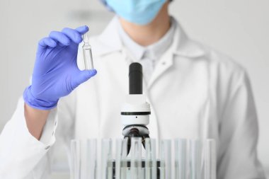 Laboratuvarda ampul ve mikroskobu olan kadın bilim adamı, yakın plan.