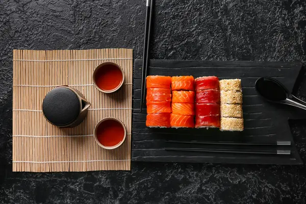 Lezzetli suşi ruloları, yemek çubukları, çaydanlık ve siyah grunge arka planda bir fincan çay.