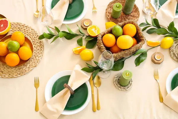 Narenciye meyveleri, yanan mumlar ve açık masa örtüsünün üzerindeki yeşil yapraklarla dolu güzel bir masa.