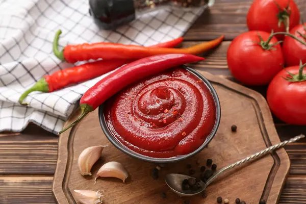 Bir kase kırmızı biber sosu ve ahşap arka planda farklı malzemeler.
