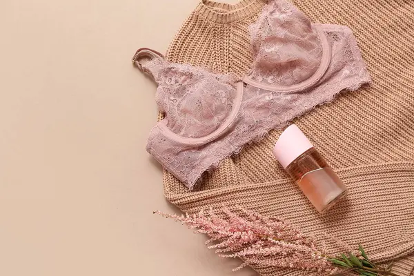 Şık dantel sutyenli kompozisyon, örgü süveter, bir şişe parfüm ve arka planda çiçek.