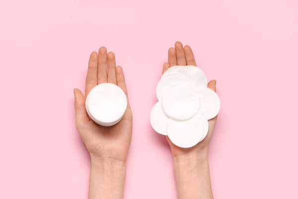 Female hands with cotton pads on pink background