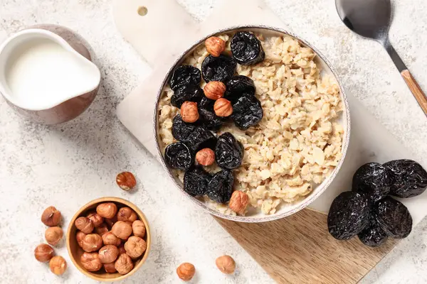 Bir kase lezzetli yulaf ezmesi, kuru erik, fındık ve beyaz Grunge arka planda bir sürahi süt.
