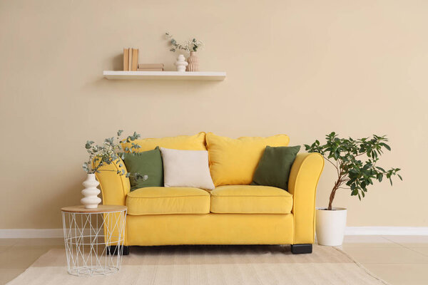 Cozy yellow sofa and coffee table with  eucalyptus branches in vase near beige wall in room