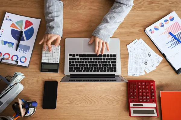 Dizüstü bilgisayar ve hesap makinesiyle çalışan kadın muhasebecinin elleri.