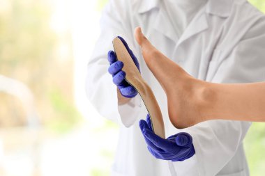 Ortopedist klinikte kadın ayağı üzerinde insole deniyor, yakın plan.