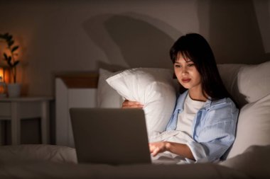 Geceleri yatak odasında dizüstü bilgisayar kullanan genç bir kadın.