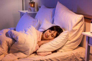 Geceleri yatak odasında battaniyenin altında uyuyan genç bir kadın.