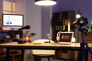 Podcaster 'ın iş yeri. Karanlık stüdyoda dizüstü bilgisayarı ve mikrofonları var.