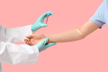 Doktorun elleri, test tüpü ve pembe arka planda kan donörü.