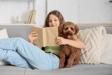 Evdeki kanepede fino köpeği okuyan genç bir kız.