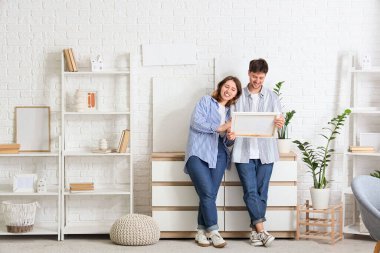 Evlerinde beyaz tuğlalı duvarda resimleri olan genç bir çift.