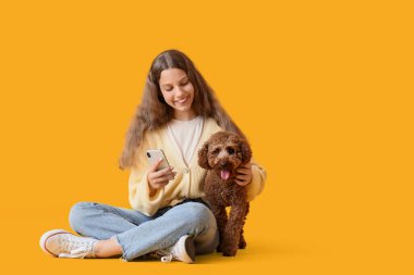 Kaniş köpekli genç kız sarı arka planda cep telefonu kullanıyor.