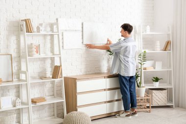 Evdeki beyaz tuğla duvara resim asan genç adam.