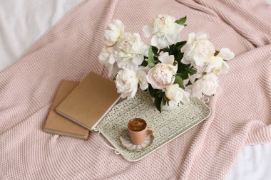 Kahve tepsisi, şakayık çiçekleri ve yatağın üstünde kitaplar.