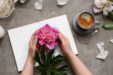 Şakayık çiçekli kadın elleri, bir fincan kahve ve arkaplan üzerine kitap.