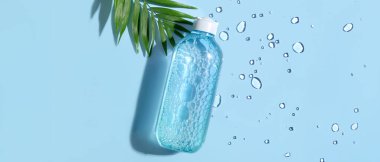 Mavi arka planda bir şişe mikiler suyu ve tropikal yaprak, yakın plan.