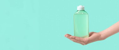 Yeşil arka planda bir şişe mikiler suyu olan kadın el, yakın plan.