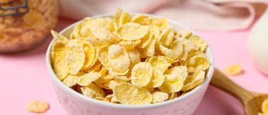 Pembe arka planda lezzetli mısır gevrekleri olan kase, yakın plan.