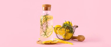 Biberiyeli bir şişe taze limonata ve pembe arka planda limonlar.