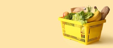 Farklı taze ürünlerle dolu sarı alışveriş sepeti ve bej arka planda elmalar