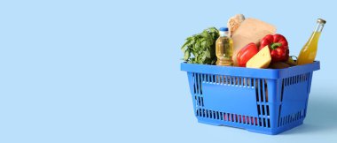 Farklı taze ürünlerle dolu mavi alışveriş sepeti ve mavi arka planda bir şişe yağ.