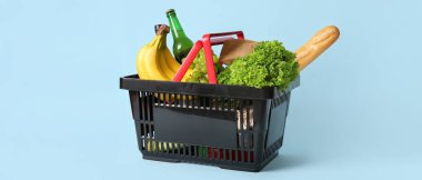 Farklı taze ürünlerle dolu siyah alışveriş sepeti ve mavi arka planda baget.