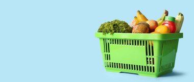 Farklı taze ürünlerle dolu yeşil alışveriş sepeti ve mavi arka planda hardal.