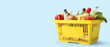 Farklı taze ürünler ve elmalarla dolu sarı alışveriş sepeti mavi arka planda