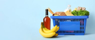 Bir şişe şarap, muz, mavi alışveriş sepeti farklı taze ürünler ve mavi arka planda bir şişe süt.