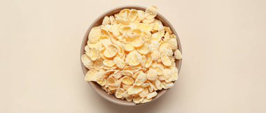 Bej arka planda lezzetli mısır gevrekleri olan kase, üst görünüm.