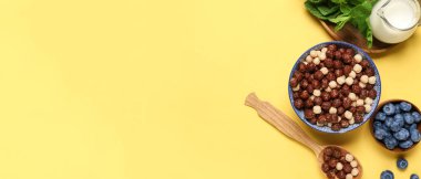 Bir kase lezzetli çikolatalı mısır topları, sarı arka planda süt ve yaban mersini ve metin için yer var.