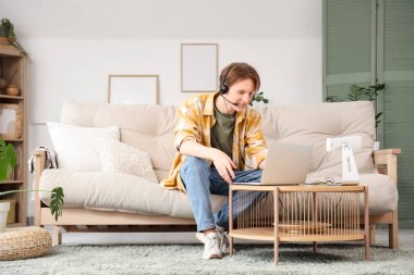 Tablet bilgisayarı, dizüstü bilgisayarı ve kulaklığı olan genç çocuk evde çalışıyor.